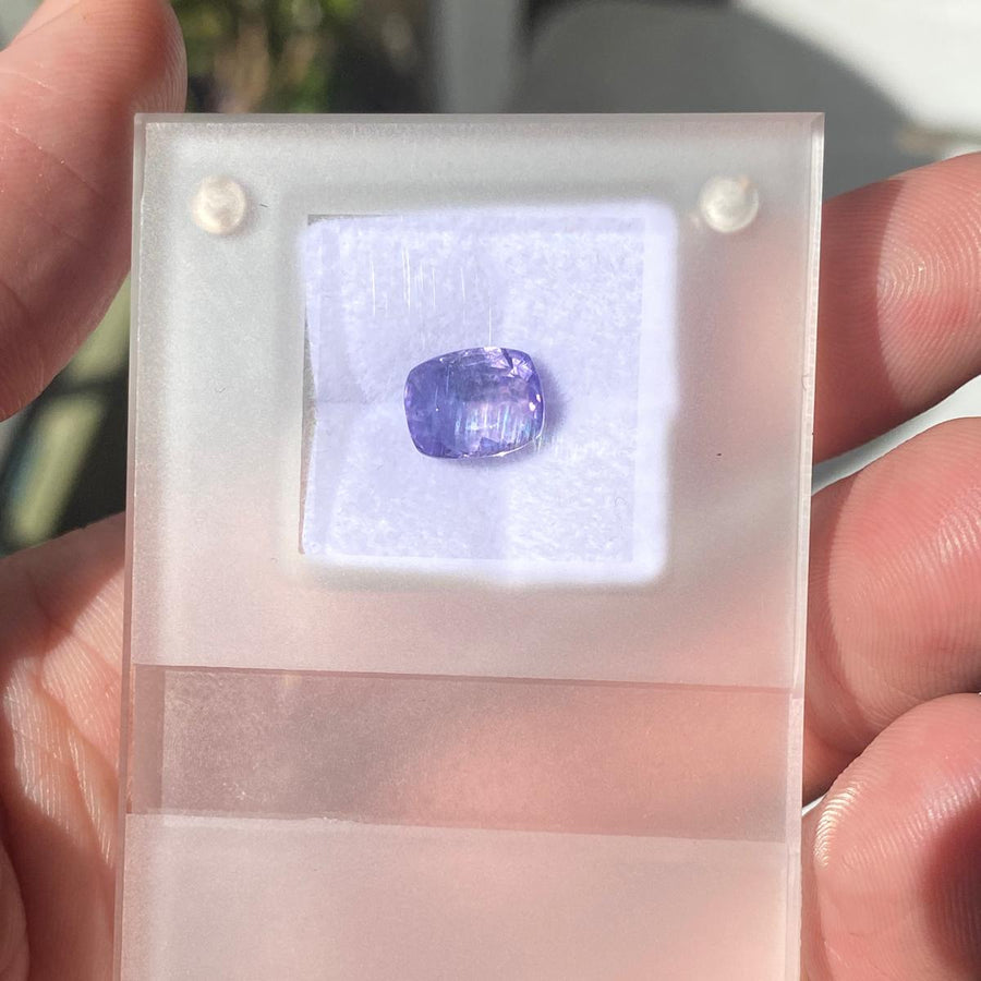 A 4.52 carat purple sapphire displayed on a translucent acrylic holder with a white insert, held in a person's hand outdoors.