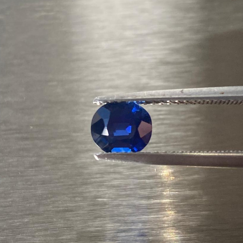 1.27 ct unheated Cambodian royal blue sapphire held in tweezers, face-up view
