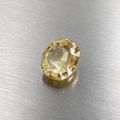 A single oval-cut yellow sapphire with a faceted surface, resting on a brushed silver metal background.