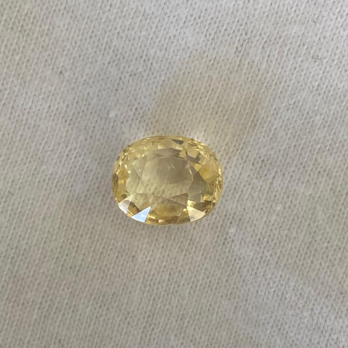 An oval-cut yellow sapphire, displayed on a textured off-white fabric background.