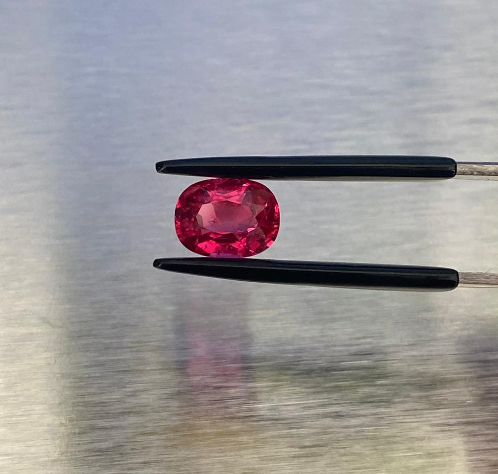 1.63 ct vivid red oval spinel, face-up view held in gemological tweezers