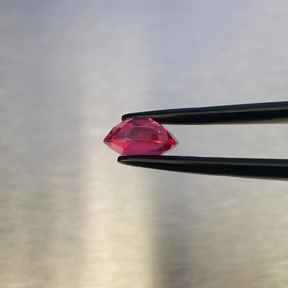 1.63 ct vivid red oval spinel, profile view held in gemological tweezers