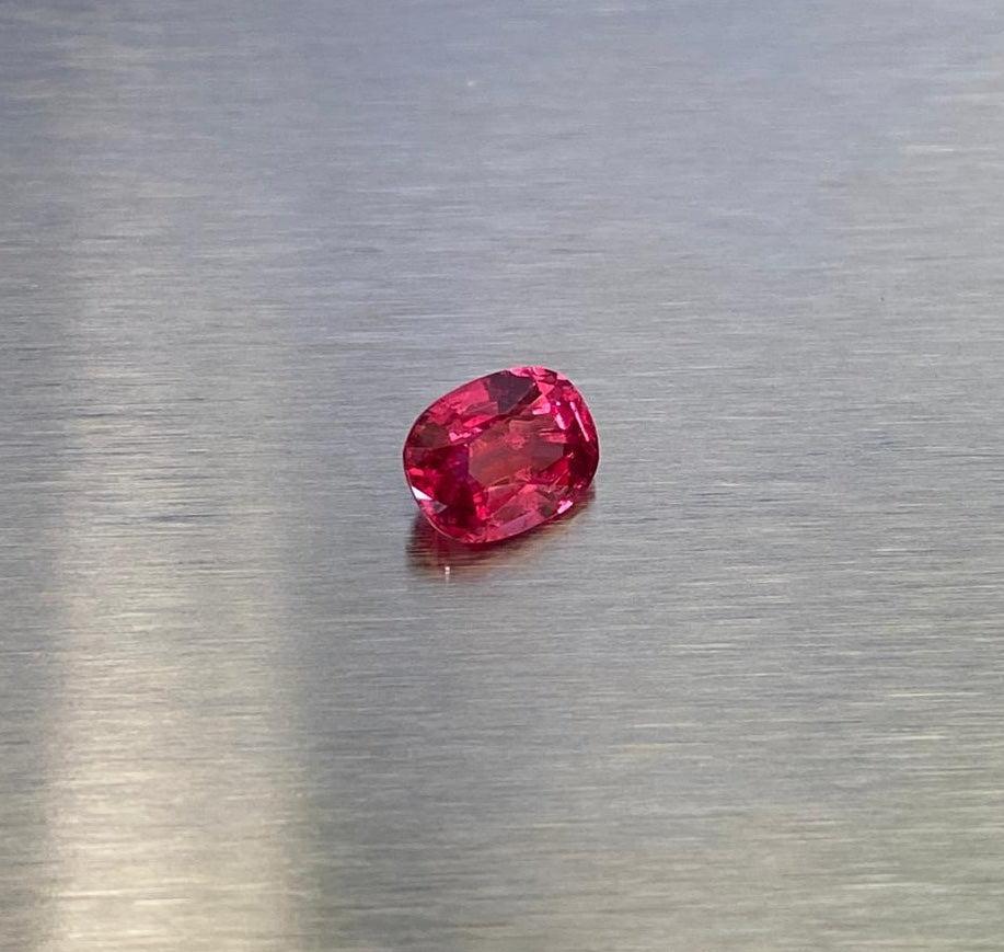 1.63 ct vivid red oval spinel, angled face-up view on metallic background