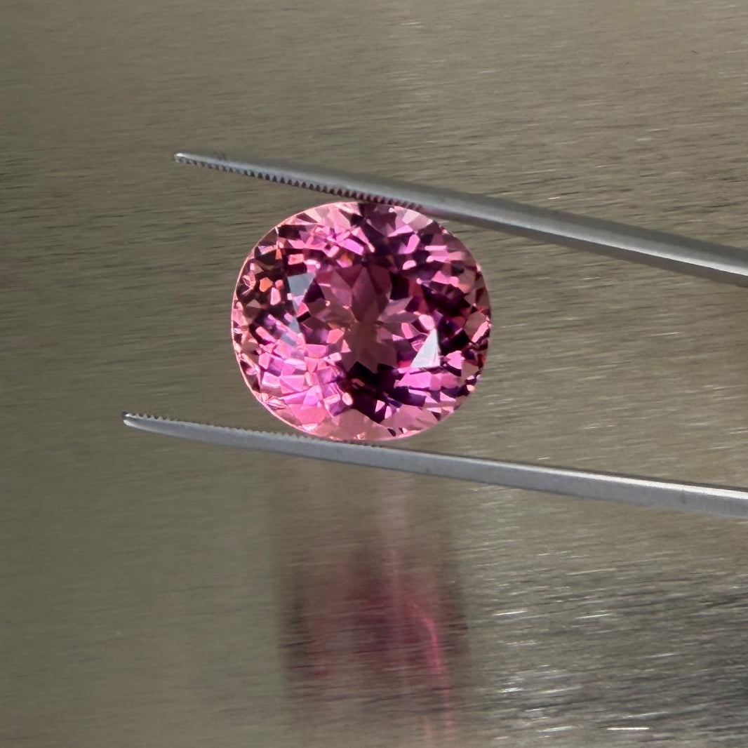 23.58 ct natural pink tourmaline held face-up in tweezers showing vibrant pink color and brilliance, Otzera OTZ-2026-01635