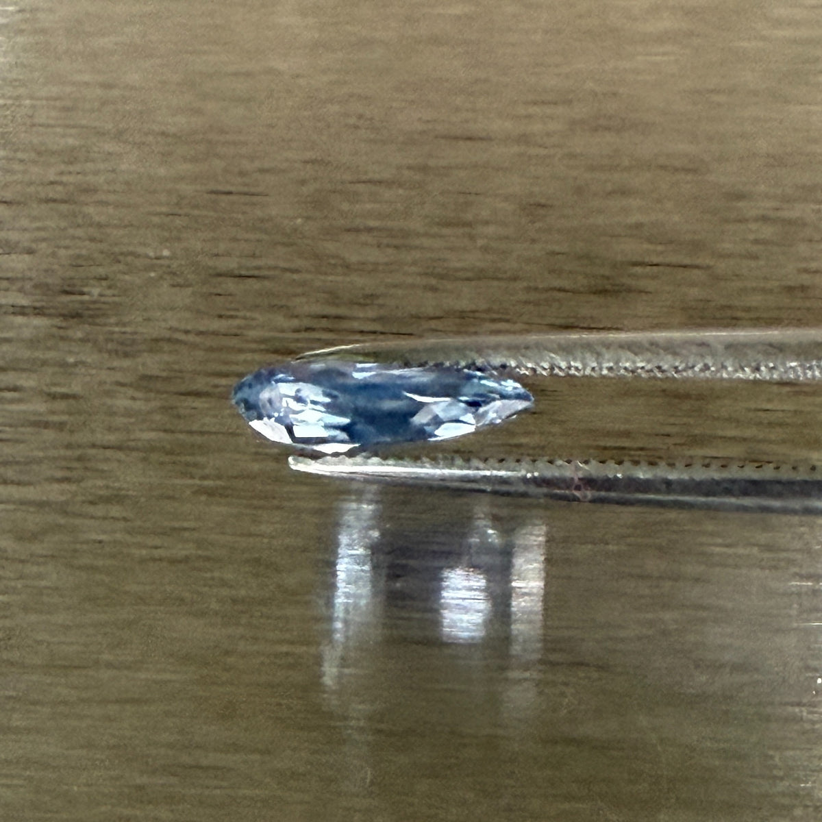 2.44 ct unheated blue sapphire held in tweezers, side profile showing shallow cut, Otzera OTZ-2026-01672