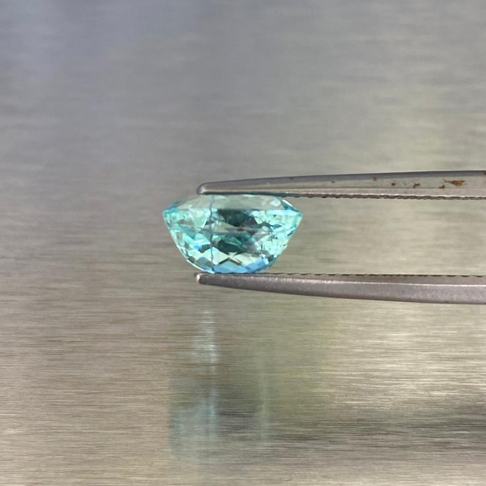 1.71 ct GIA-certified Paraiba-type tourmaline held in tweezers, side profile showing the oval modified brilliant cut.