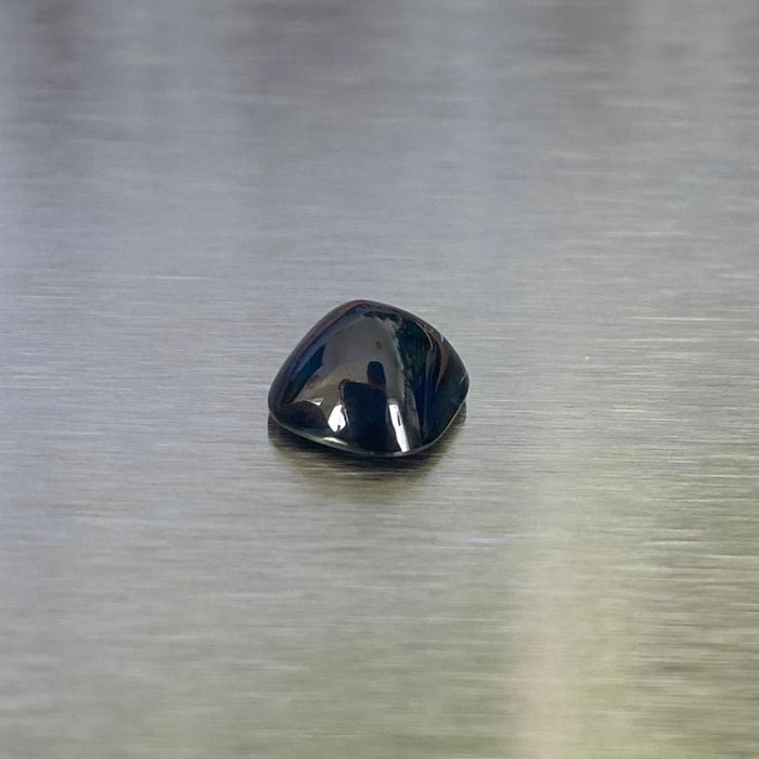 2.41 ct unheated Australian blue sapphire, cushion sugarloaf cabochon front view on a brushed silver background.