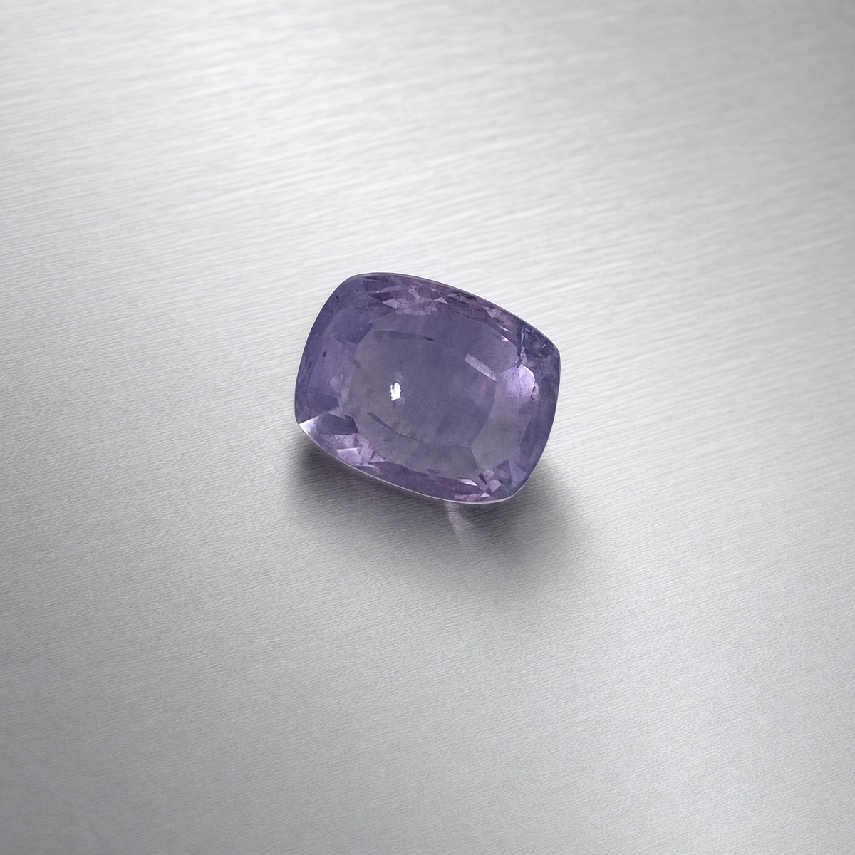 A cushion-cut purple sapphire, displayed on a brushed silver metal surface.