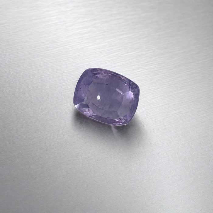 A cushion-cut purple sapphire, displayed on a brushed silver metal surface.